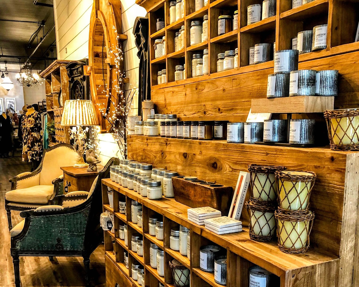 An organized and warmly lit interior of a high-end boutique in downtown McMinnville, featuring wooden shelves stocked with various jarred candles, home fragrances, and rustic decor alongside plush seating.