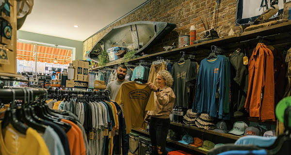 A bright and rustic interior of an outdoor retail store in McMinnville, TN, featuring exposed brick walls, a wooden canoe suspended from the ceiling, and racks of high-quality outdoor apparel and gear.