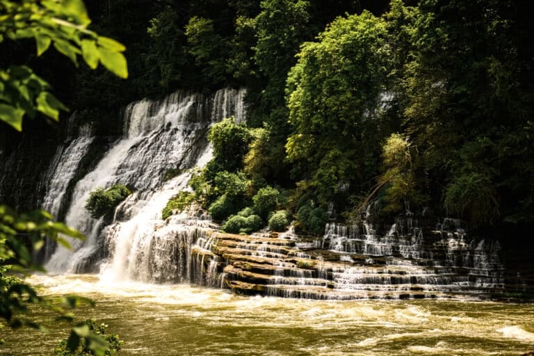 Tiered waterfall cascading over limestone at Rock Island State Park near McMinnville, TN, surrounded by lush green forest.