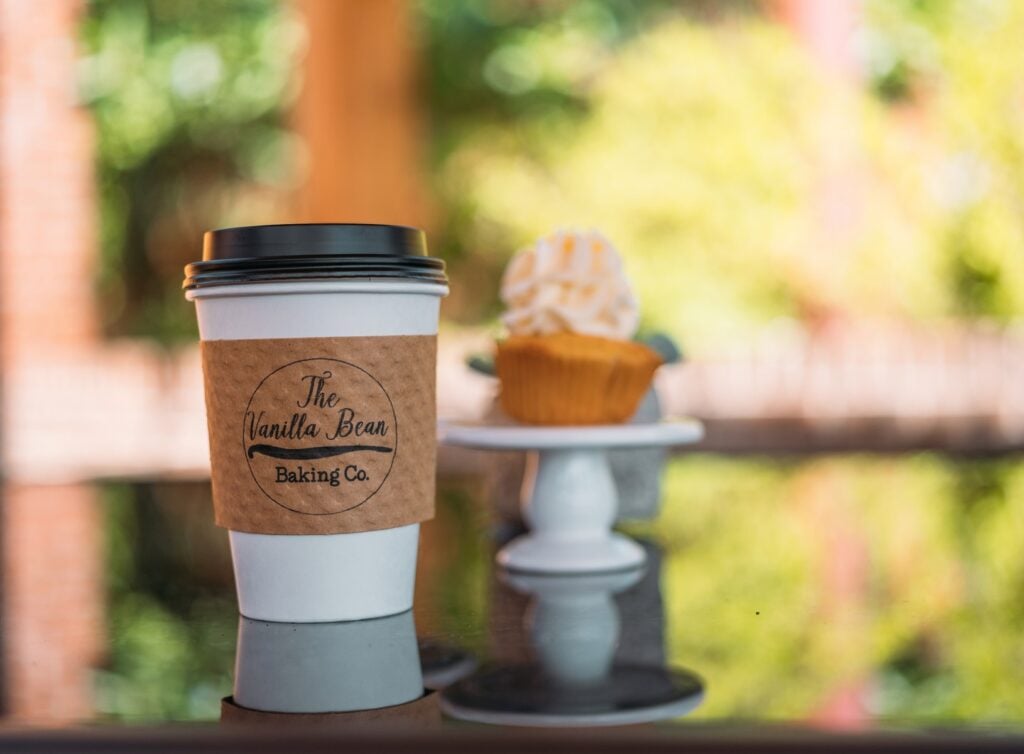 A bright, cozy bakery interior on historic Main Street with a glass display case filled with gourmet cupcakes and golden-brown cinnamon rolls.