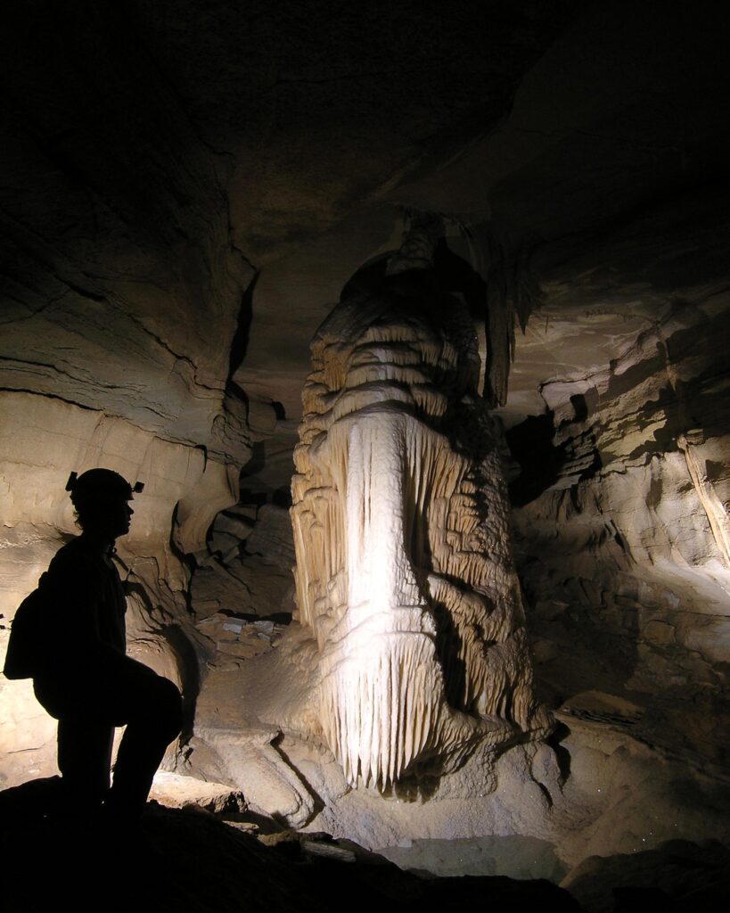 A dramatic silhouette of a caver standing before the massive, glowing Monument Pillar formation inside the ancient limestone passages of Cumberland Caverns near McMinnville, TN.