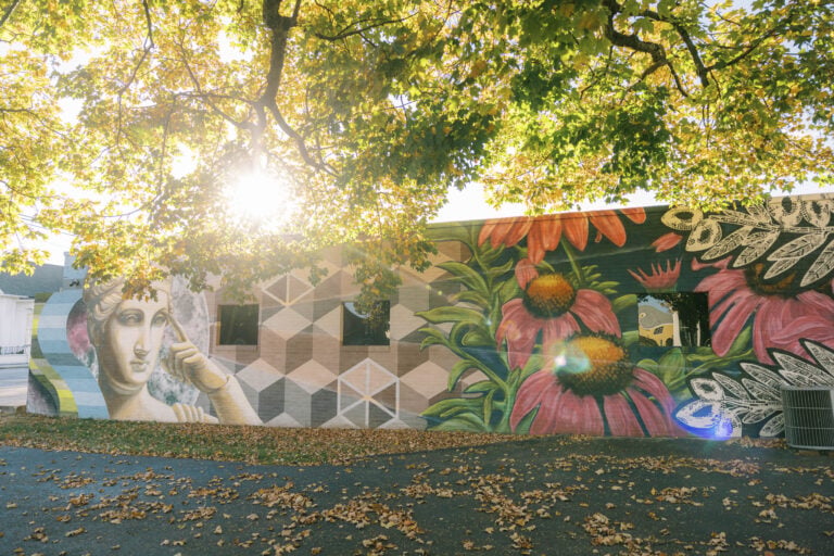 A vibrant outdoor mural in McMinnville featuring Hebe, goddess of youth, with celestial symbols and flowing lines representing the Barren Fork and Collins rivers.