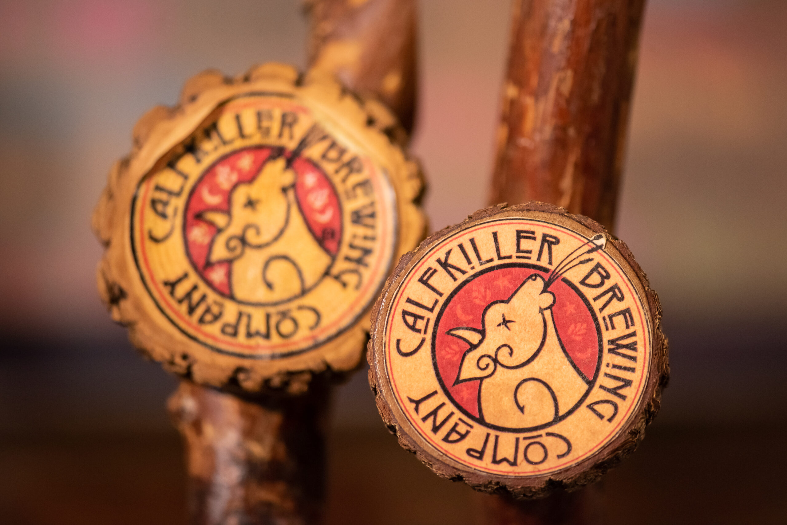 A detailed close-up of two rustic, wood-carved tap handles featuring the distinctive goat logo of the local Calfkiller Brewing Company.