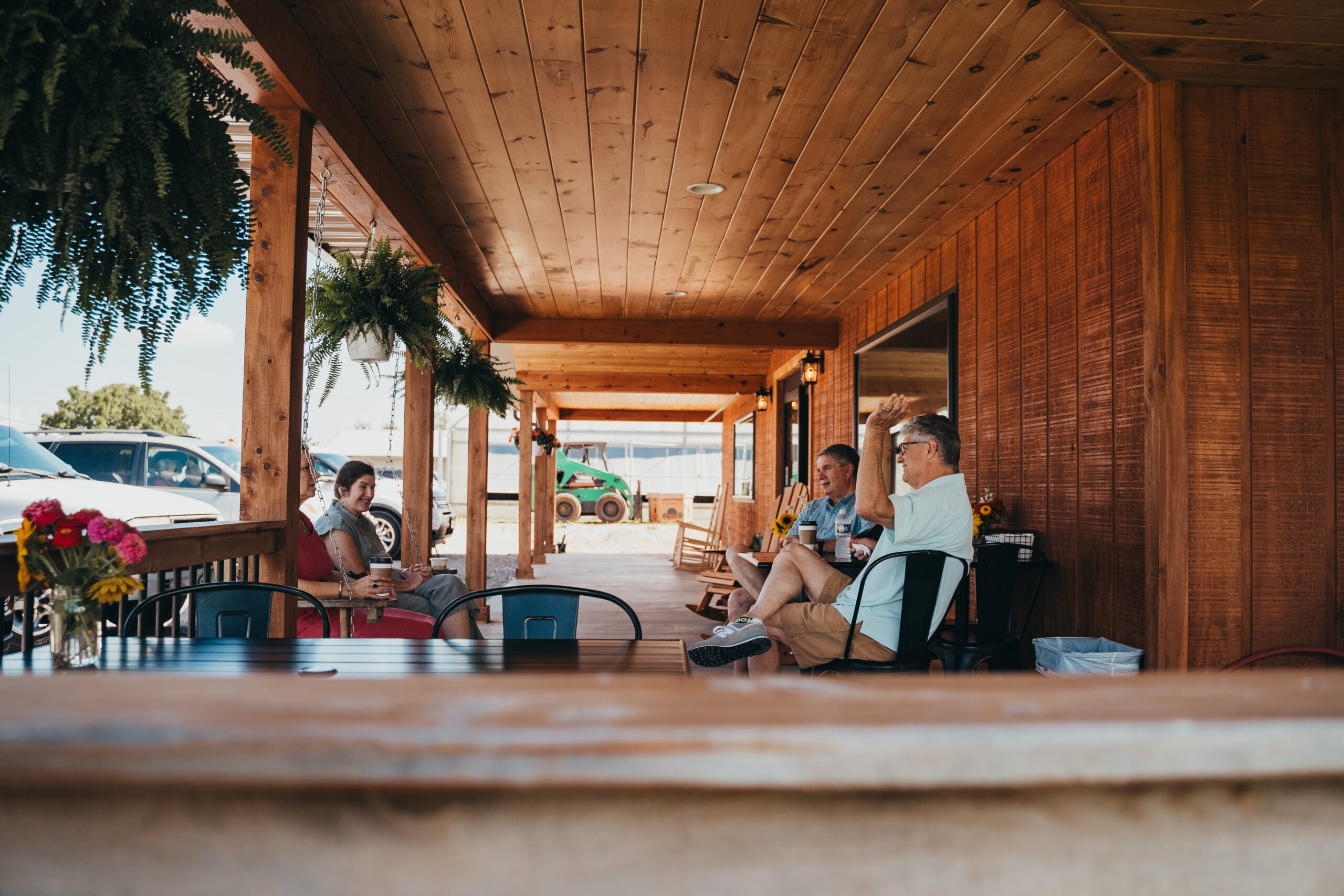 A scenic view of a clean, modern farm market building with a large covered porch, situated against a backdrop of the rolling green hills and blue skies of Warren County.