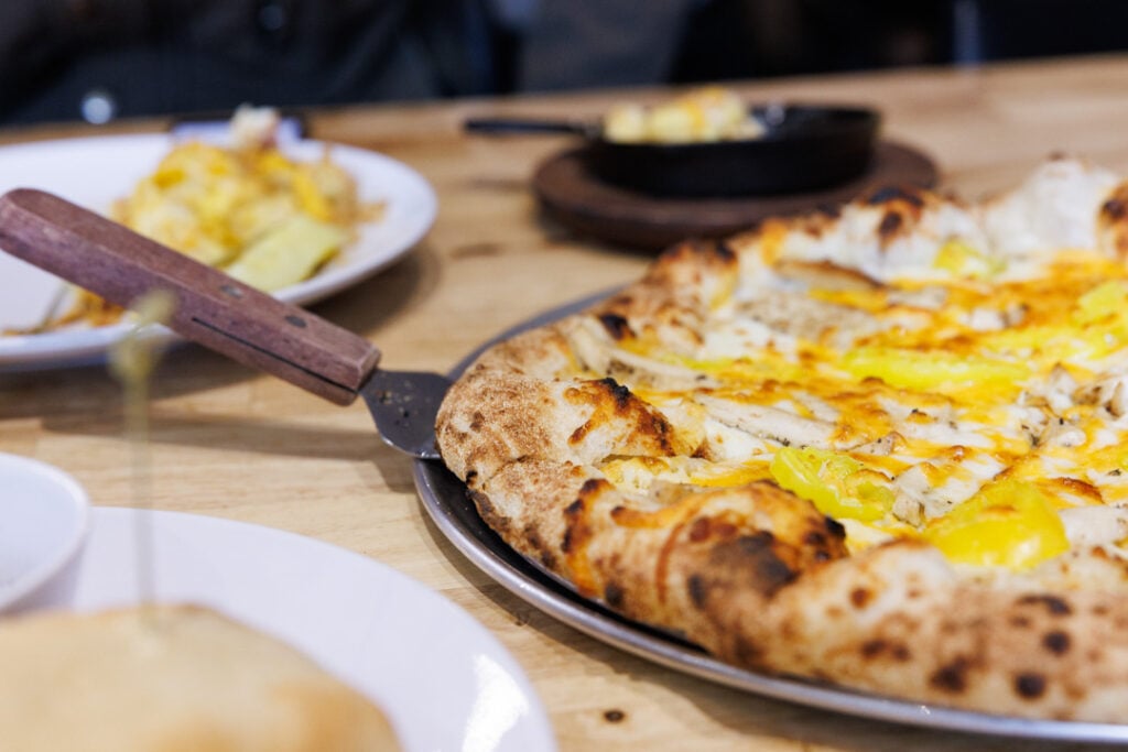 A close-up of a wood-fired pizza with banana peppers and chicken on a wooden table at Begonia's in downtown McMinnville.