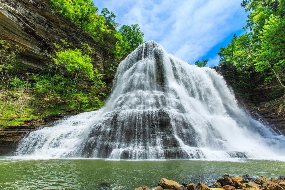 A massive waterfall dropping over a sheer cliff into a river gorge surrounded by lush forest.