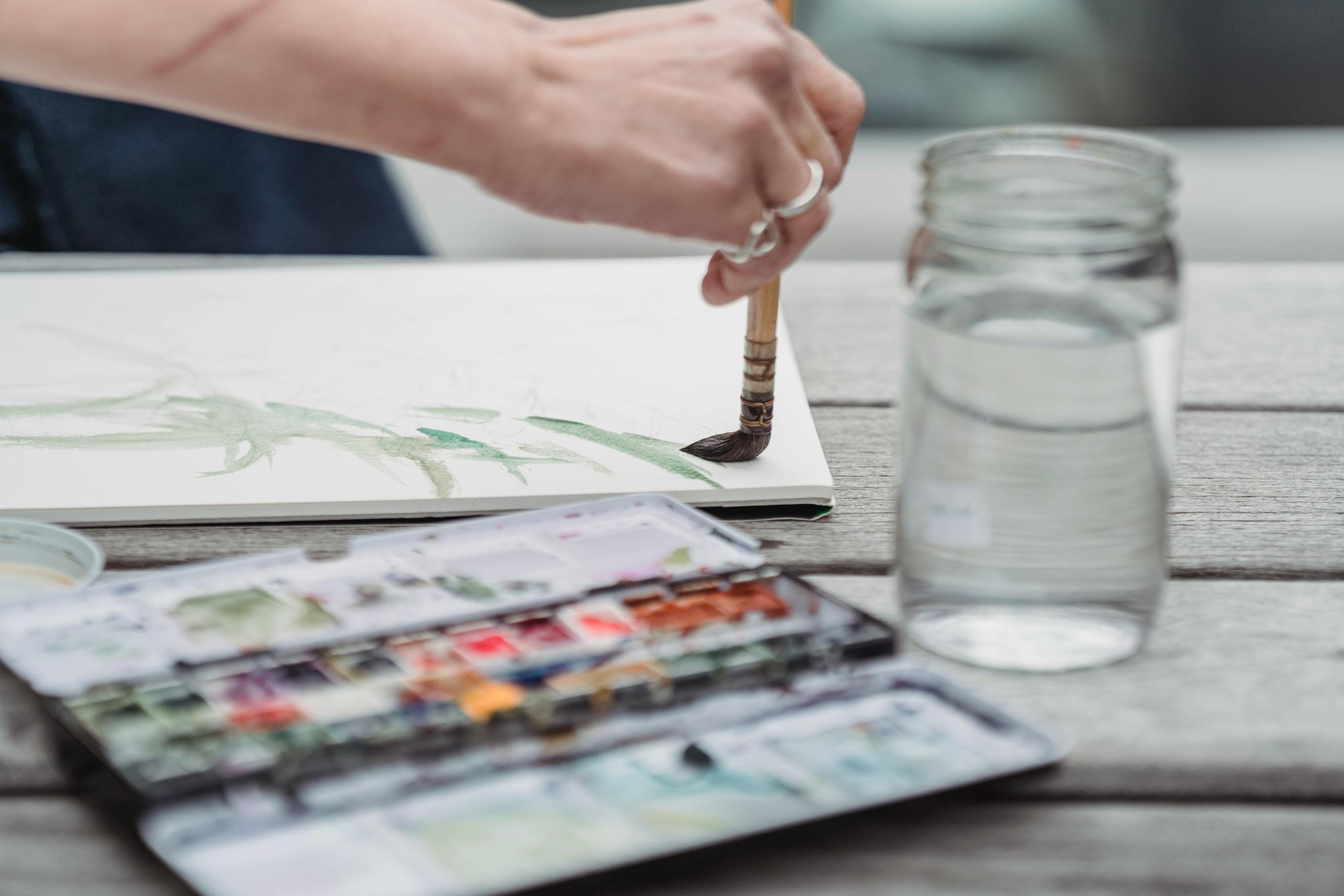 Artist's hand painting with watercolors in natural light. Creative process captured outdoors.